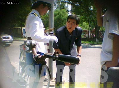 A policewoman issues a man a traffic ticket. Many citizens who do not want to pay for a ticket try to bribe the officers for a lesser amount of money. Working as a traffic officer is known to be lucrative, and for this reason policewomen must secure their positions through connections to ranked officials.[Gu Gwang-ho, 2011]