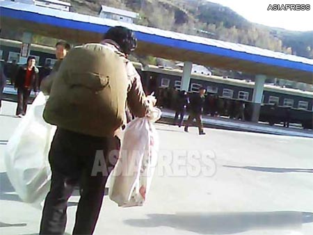 A woman with a backpack hurries to catch the train. She runs towards the station while humping a pack bursting at the seams, and bags in each of her hands. (Taken in a northern border city of North Korea. October. 2013)　ASIAPRESS