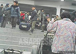 A man and woman emerge from the entrance gate of the station, each grasping a strap of a bag bursting at the seams. The railway station is usually the best place for porters to solicit customers. (Pyongsong Railway Station. South Pyongan Province. September, 2013) ASIAPRESS