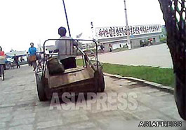 A female porter is pulling a large handcart. The slogan-board on the right reads, "Make the Great Kim Il-sung's nation and Kim Jong-il's Korea revered by the world!" (Chongjin. North Hamkyung Province. September, 2013) ASIAPRESS