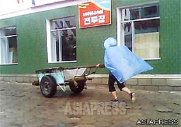 A woman in a raincoat pushes a handcart. (In a northern Sino-Korea border city. August, 2013) ASIAPRESS