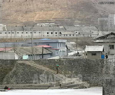 A local woman walks down to the riverbank to wash clothes. The small building on the right side of the photo is a watch house of the border guard. (Taken from Chinese side of the river. Changbai, Jilin. 21/March/2014) ASIAPRESS 