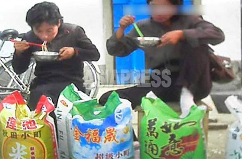 A Photo taken in the northern border town, near China. Local women eat noodles, taking a break from selling rice imported from China. Chinese characters on the rice sacks make the content's origin unambiguous. (October, 2013) ASIAPRESS